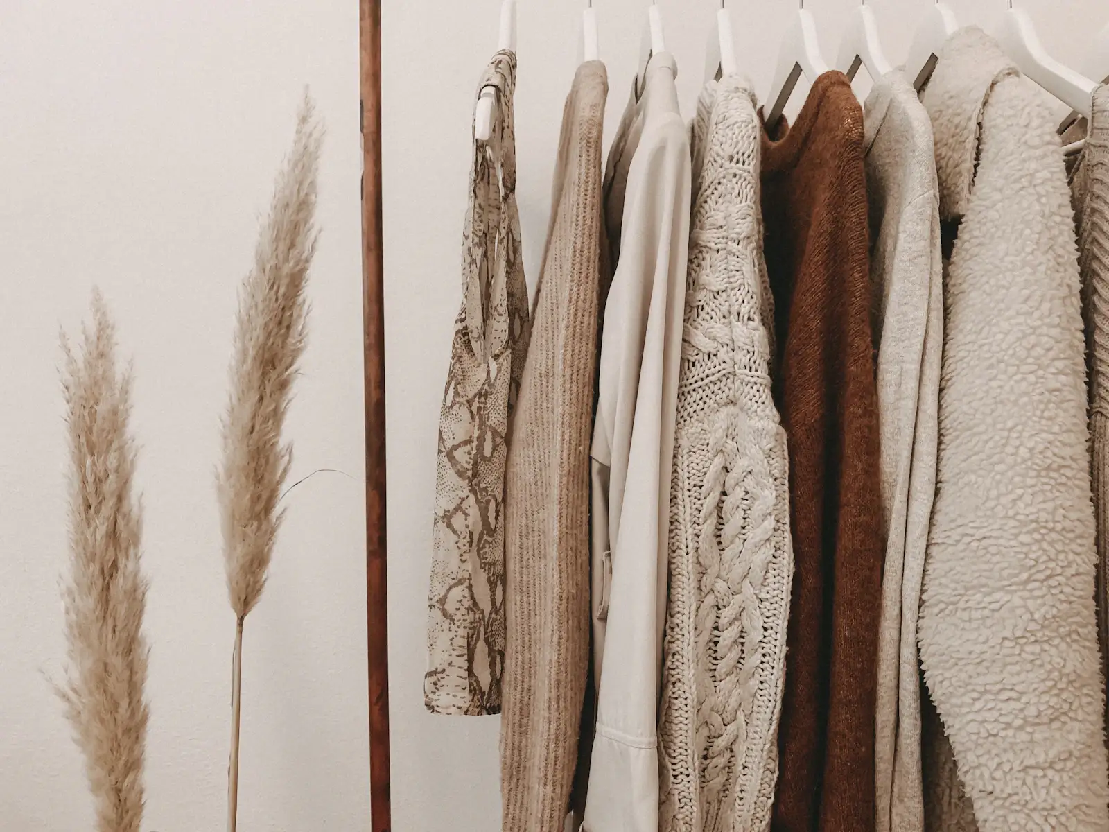 A rail of undyed and natural-toned garments in daylight beside dried grasses